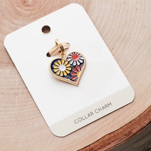 May include: Gold heart-shaped collar charm with a blue enamel background and colorful floral design. The charm is on a white card with the text "COLLAR CHARM".