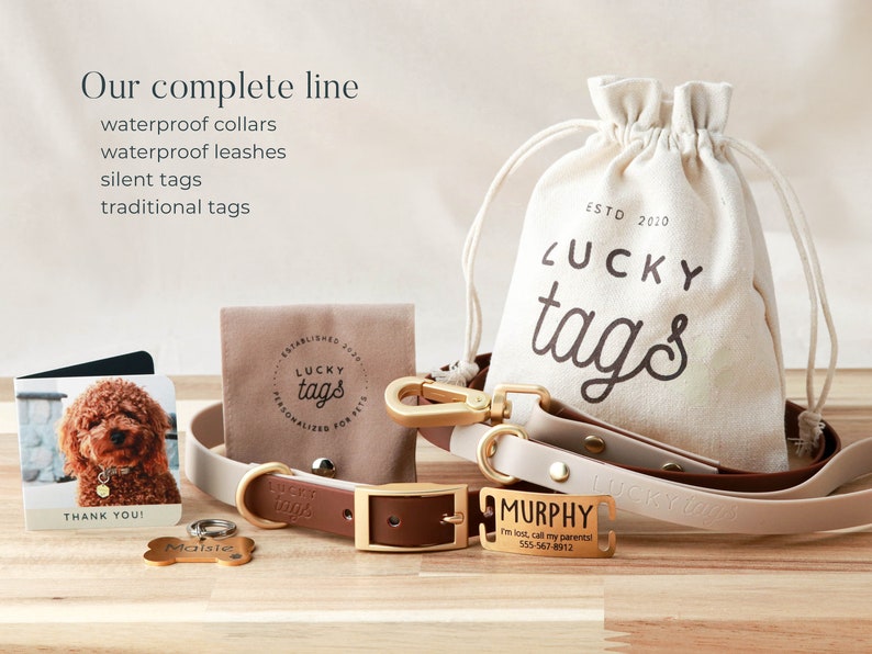 May include: A set of dog accessories from Lucky Tags, including a brown leather collar with a gold buckle, a beige and brown leather leash with a gold clasp, a gold dog tag with the name "Murphy" engraved on it, and a small brown pouch with the Lucky Tags logo. The pouch is made of canvas and has a drawstring closure. The text "ESTD 2010" is printed on the pouch.