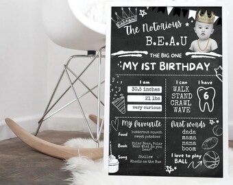May include: Black and white chalkboard style first birthday sign with a photo of a baby boy wearing a gold chain. The sign says "The Notorious B.E.A.U. The Big One My 1st Birthday". It also includes the baby's height, weight, and favorite things.