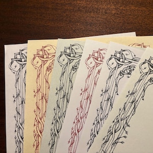 May include: A set of six rectangular stationery sheets featuring a decorative border design of intertwined vines and knotwork. The papers are in various colors including white, cream, and light green, with the border printed in black or red ink.