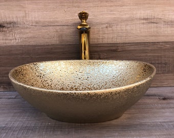May include: A gold-colored, oval-shaped vessel sink with a textured surface. A gold faucet is mounted on the sink. The sink is a bathroom fixture.