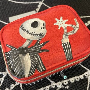 May include: Red zippered pouch with a black and white illustration of Jack Skellington from The Nightmare Before Christmas. The illustration shows Jack holding a snowflake.