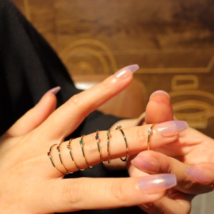 May include: A set of gold rings with small colourful gemstones. The rings are stacked on a person's finger.