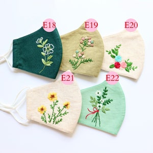 May include: Five different fabric face masks with embroidered floral designs. The masks are in various colours, including green, beige, and light green. The embroidery designs include flowers, leaves, and stems.