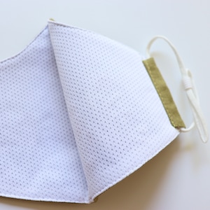 May include: A green fabric face mask with a white mesh lining. The mask has a white elastic strap.