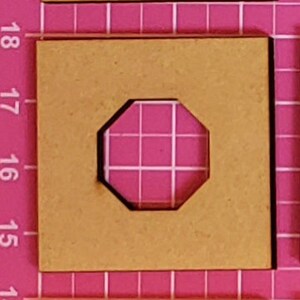 May include: A square, light brown wooden tile with a pink, octagonal cutout in the center. The cutout has a white grid pattern. The tile is on a pink grid background.