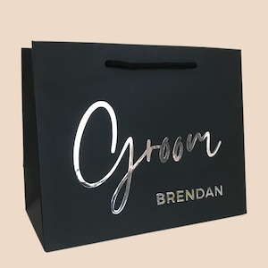 May include: Black gift bag with the word "Groom" in silver script and the name "Brendan" in silver block letters. The bag has a black rope handle.