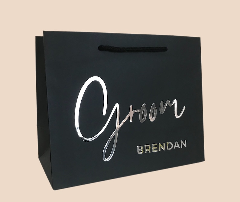 May include: Black gift bag with the word "Groom" in silver script and the name "Brendan" in silver block letters. The bag has a black rope handle.