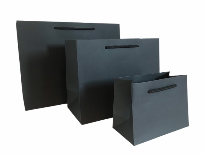 May include: Three gray gift bags of varying sizes are arranged in a row. Each bag has a matching black rope handle. The bags are made of a glossy paper material and are empty.