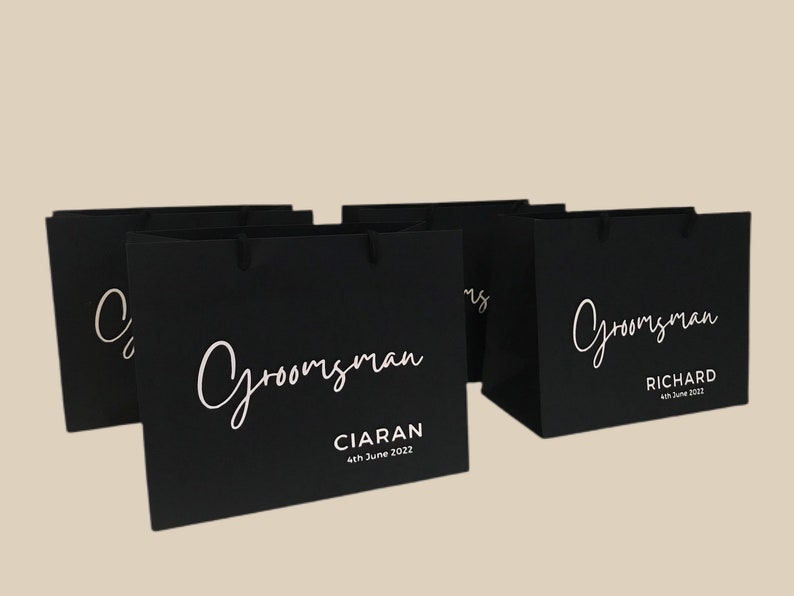 May include: Black gift bags with white text that reads "Groomsman" in a script font. One bag has the name "Ciaran" and the date "4th June 2022". Another bag has the name "Richard" and the date "4th June 2022".