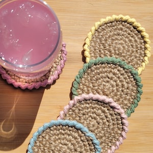 May include: Four crocheted coasters with a jute center and a colorful crocheted border. The coasters are in shades of yellow, green, pink, and blue.