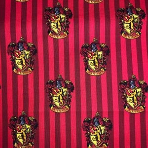 May include: Red and gold fabric with a repeating pattern of the Gryffindor house crest from the Harry Potter series. The crest features a lion, a castle, and the words "Gryffindor" in a banner.