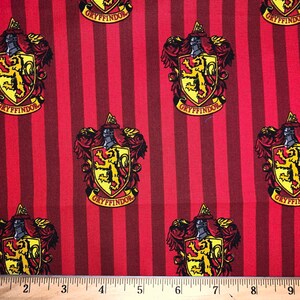 May include: Red and gold fabric with a repeating pattern of the Gryffindor house crest from the Harry Potter series. The crest features a lion, a shield, and the words "Gryffindor" in a banner.