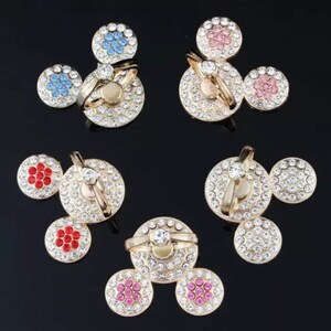 Może przedstawiać: Zestaw czterech uchwyt&oacute;w na pierścienie do telefonu z wzorem Myszki Miki. Każdy uchwyt ma inny kolor środka z kryształk&oacute;w i przezroczysty pierścień.