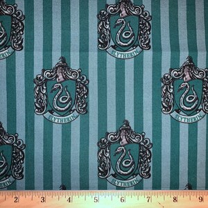 May include: Green and white striped fabric with a repeating pattern of the Hogwarts house crest for Slytherin. The crest features a silver snake with red eyes and the words "Slytherin" in a black banner.