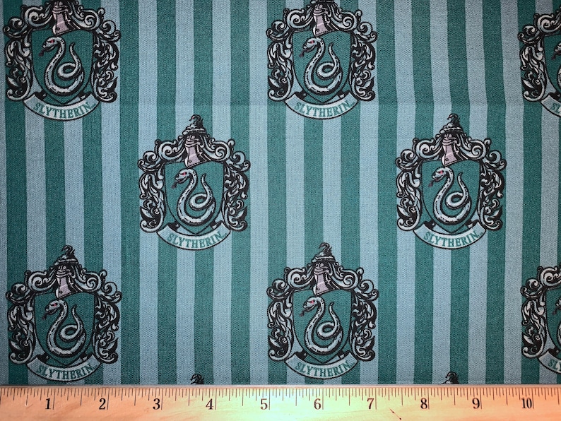 May include: Green and white striped fabric with a repeating pattern of the Hogwarts house crest for Slytherin. The crest features a silver snake with red eyes and the words "Slytherin" in a black banner.