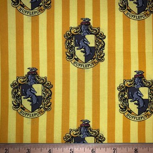 May include: Yellow and brown fabric with a repeating pattern of the Hufflepuff house crest from the Harry Potter series. The crest features a badger, a black and yellow shield, and the words "Hufflepuff" in a gold banner.