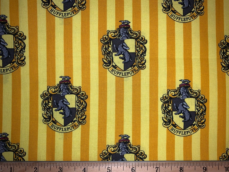May include: Yellow and brown fabric with a repeating pattern of the Hufflepuff house crest from the Harry Potter series. The crest features a badger, a black and yellow shield, and the words "Hufflepuff" in a gold banner.