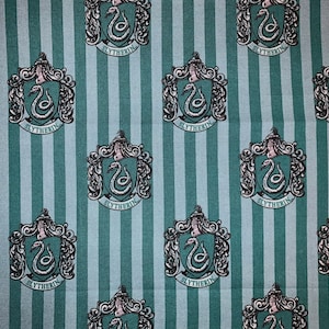 May include: Green and blue striped fabric with a repeating pattern of the Hogwarts house crest for Slytherin. The crest features a silver snake with the word "Slytherin" written below it.