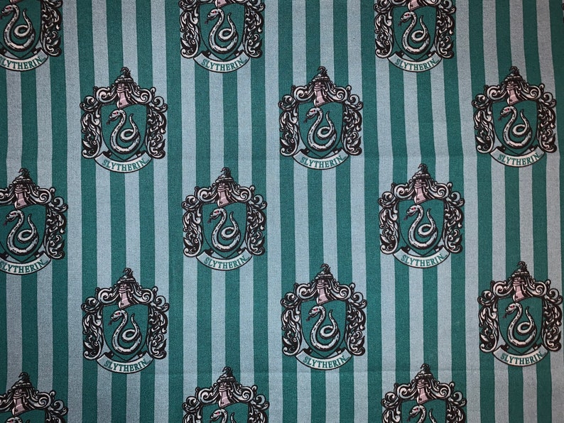 May include: Green and blue striped fabric with a repeating pattern of the Hogwarts house crest for Slytherin. The crest features a silver snake with the word "Slytherin" written below it.