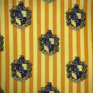 May include: Yellow and white striped fabric with a repeating pattern of the Hufflepuff house crest from the Harry Potter series. The crest features a badger, the house colors, and the words "Hufflepuff" in a banner.