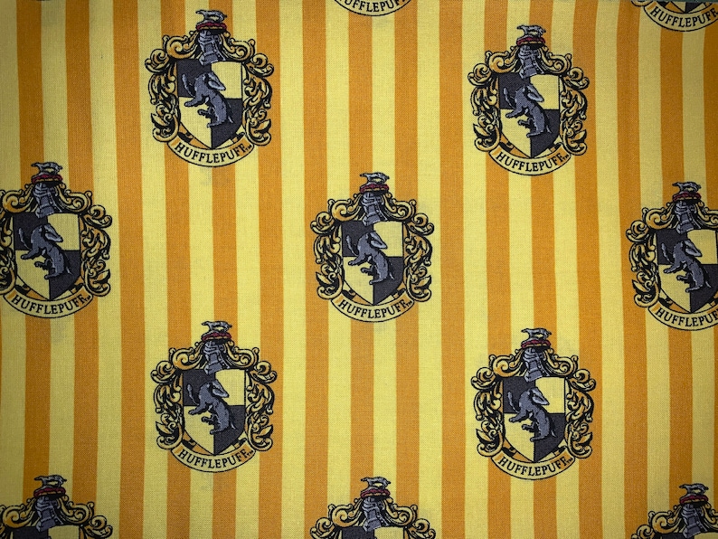 May include: Yellow and white striped fabric with a repeating pattern of the Hufflepuff house crest from the Harry Potter series. The crest features a badger, the house colors, and the words "Hufflepuff" in a banner.