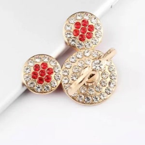 May include: Gold phone ring holder with a spinning design. The ring is decorated with clear and red rhinestones.