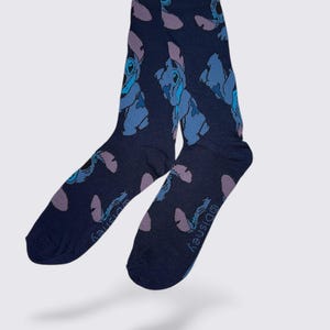 May include: A pair of navy blue socks featuring a repeating pattern of a blue cartoon character with purple accents. The socks have the Disney logo printed on the side.
