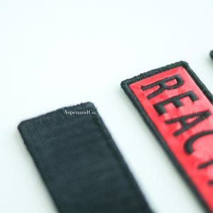 Three dog patches with black stitching. The first patch is showing the back hook side of the patch. The second patch is red with the text 'REACTIVE.' The third patch is green with the text 'REACTIVE.'