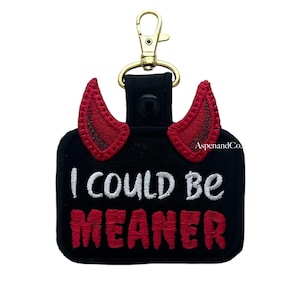 May include: Black hand sanitizer holder with red devil horns and gold-colored clip. The text "I COULD BE MEANER" is embroidered in white and red. The brand name "AspenandCo." is also visible.