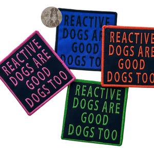 May include: Four embroidered patches with the text "REACTIVE DOGS ARE GOOD DOGS TOO". The patches are in various colors: pink, blue, orange, and green. The patches are square or rectangular with a black background.
