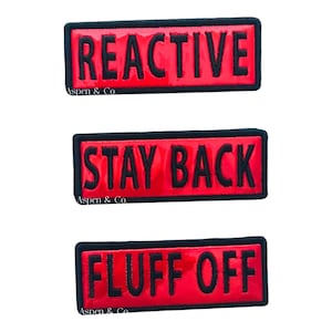 May include: Three rectangular patches with black borders and text. The top patch reads "REACTIVE", the middle patch reads "STAY BACK", and the bottom patch reads "FLUFF OFF". All patches have a red background and black text.