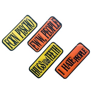 May include: Four rectangular patches with black borders and text. The patches are yellow and orange. The yellow patches read "FCKN PYSCHO" and "HUGS w/ TEETH". The orange patches read "EWW, PEOPLE" and "I HATE PEOPLE".