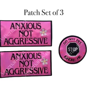 May include: A set of three embroidered patches. Two rectangular patches are hot pink with the words "ANXIOUS NOT AGGRESSIVE" in black, and a small flower. The third patch is round, pink, and says "DO NOT PET STOP IGNORE ME".