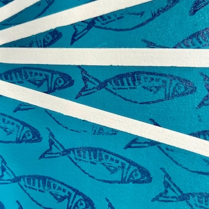 May include: A stack of teal blue cards with a repeating pattern of dark blue fish printed on them. The cards are separated by white strips.