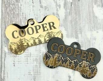 Peut inclure: Deux médailles pour chien en forme d'os avec le nom "COOPER" gravé dessus. Une médaille est dorée avec une scène de montagne noire, et l'autre est noire avec une scène de montagne dorée.
