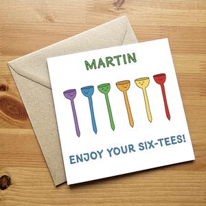 May include: A white card with the name "MARTIN" written in green text. The card has a rainbow of six golf tees with smiley faces on them. The text "ENJOY YOUR SIX-TEES!" is written in blue text at the bottom of the card.