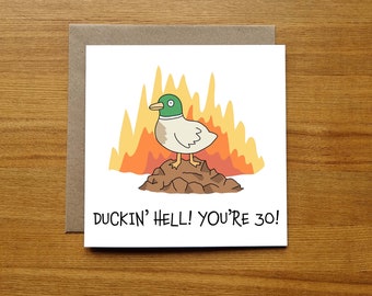 May include: A white card with a cartoon duck standing on a pile of dirt in front of a yellow and orange fire. The text on the card reads "Duckin' Hell! You're 30!"