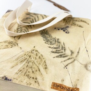 Op de afbeelding: Een beige canvas draagtas met een natuurlijk kurken label waarop "ESPONTÁNEA" staat. De tas heeft een natuurlijke, organische uitstraling en heeft een ontwerp van donkergroene varenbladeren die op de stof zijn gedrukt.