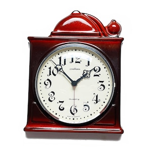 Puede incluir: Un reloj de cuarzo de estilo vintage, de color marrón rojizo, con un marco cuadrado y una parte superior abovedada. La esfera del reloj es blanca con números y manecillas negras. La palabra "pallas" está impresa encima del centro de la esfera.