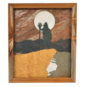 May include: A framed artwork depicting a silhouette of a figure holding a trident, standing on a cliff with a full moon in the background. The artwork is made of various shades of brown, gray, and white stone.