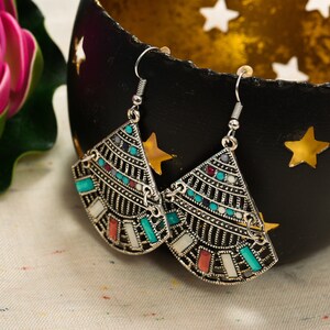 May include: A pair of silver earrings with a geometric design. The earrings are decorated with turquoise, red, and white stones.