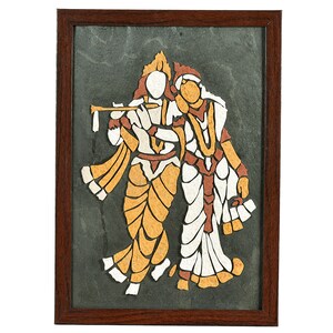 May include: A framed artwork depicting two figures in traditional attire. The figures are rendered in shades of white, tan, and brown against a dark gray background. One figure holds a flute. The artwork is encased in a dark brown wooden frame.