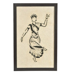May include: Framed artwork featuring a black and white illustration of a dancing figure in traditional Indian attire. The figure is depicted in a dynamic pose, with one leg raised and arms outstretched. The artwork is set against a beige background and framed in a dark brown frame.