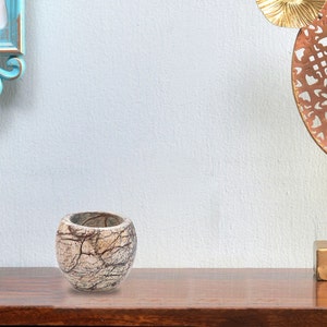 May include: A small, round, white marble planter with brown veins. The planter is sitting on a wooden surface.