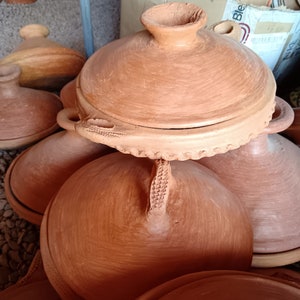 May include: A collection of handmade terracotta tagines, featuring rounded bases and domed lids with handles. The tagines are a warm, earthy brown color, showcasing traditional craftsmanship. Some lids have decorative edges.