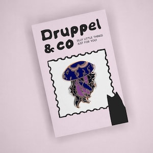 May include: A metal enamel pin shaped like a jellyfish with a dark blue bell and purple tentacles, displayed on a light pink backing card. The card features the text Druppel & CO SILLY LITTLE THINGS JUST FOR YOU! and a black cat silhouette.