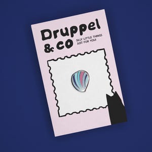 May include: A teardrop-shaped enamel pin with vertical stripes in shades of blue, pink, and white, attached to a light pink backing card. The card features the text Druppel & CO SILLY LITTLE THINGS JUST FOR YOU! and a black cat silhouette.