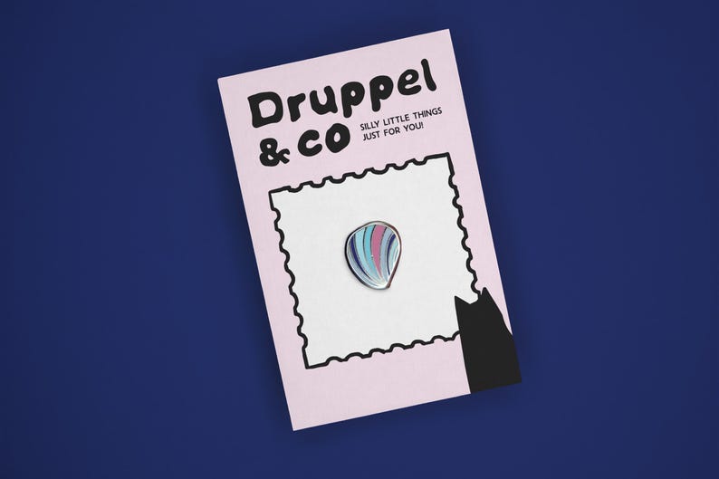 May include: A teardrop-shaped enamel pin with vertical stripes in shades of blue, pink, and white, attached to a light pink backing card. The card features the text Druppel & CO SILLY LITTLE THINGS JUST FOR YOU! and a black cat silhouette.