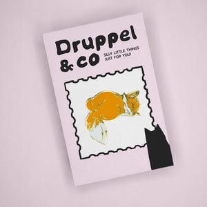 May include: A rectangular light pink card featuring the black text Druppel & CO SILLY LITTLE THINGS JUST FOR YOU! and a central white square with a black serrated border containing an orange fox enamel pin with a white tail tip and ears.